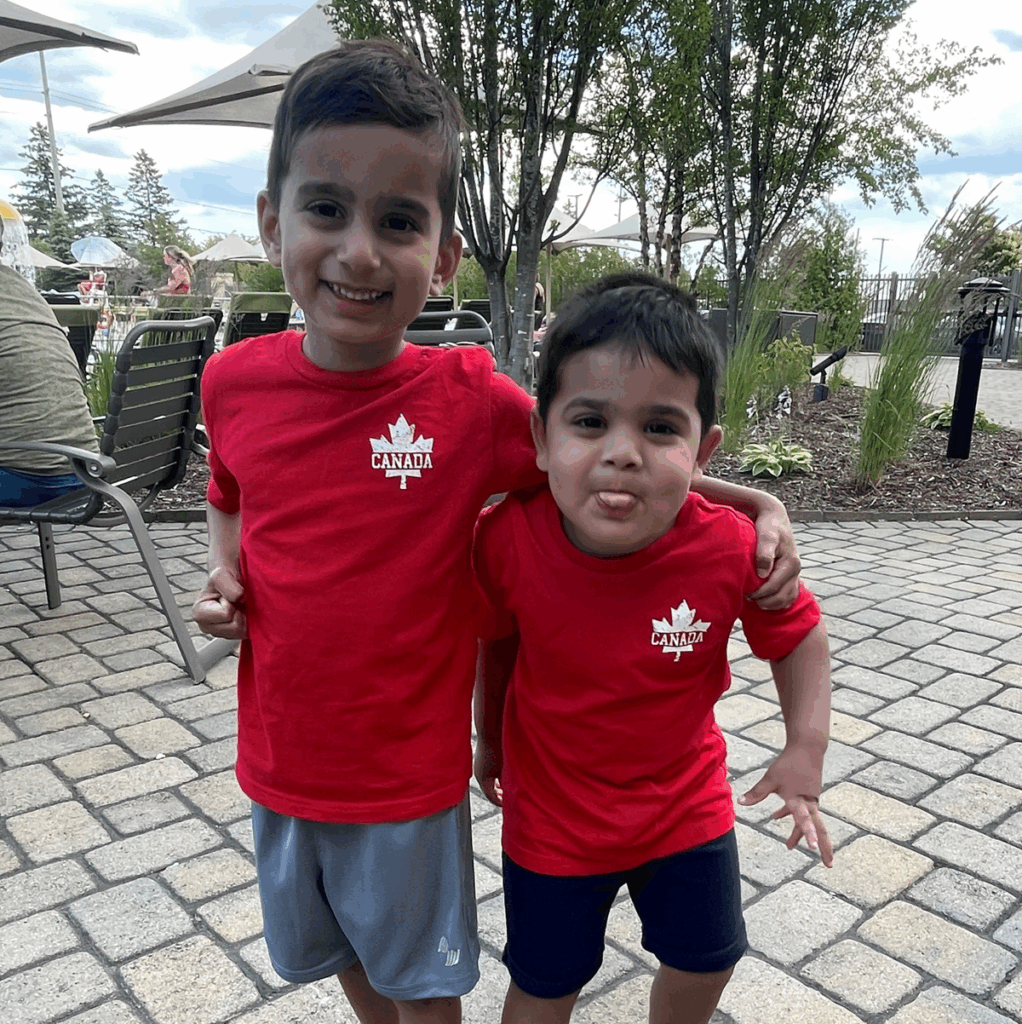 A young child smiles with his arm slung over his younger brother's shoulder.